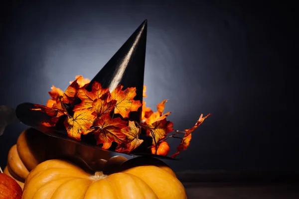 Auf schwarzem Hintergrund liegen orangefarbene Kürbisse und ein schwarzer Hexenhut mit rot-gelben Herbstblättern — Stockfoto