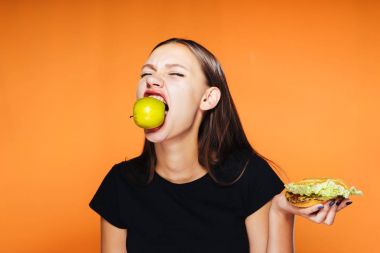 Bir kız bir elma ağzını ve hamburger elinde tutan