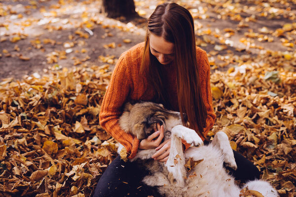 A girl hugs her dog lying in the autumn foliage