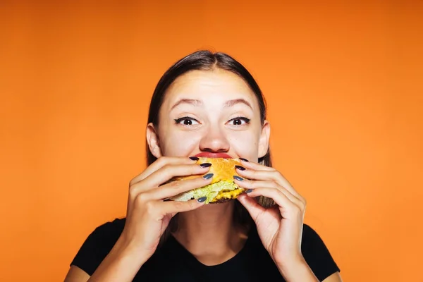 그녀의 햄버거를 먹는 오렌지 배경에 행복 한 여자 — 스톡 사진