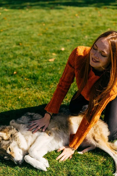 Leende flicka ligger på gräset i parken med sin hund — Stockfoto