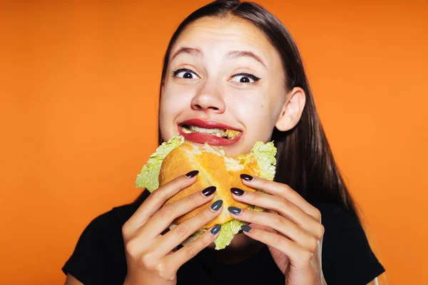 Дівчина з великим бургер в руках посміхається, роблячи укус — стокове фото