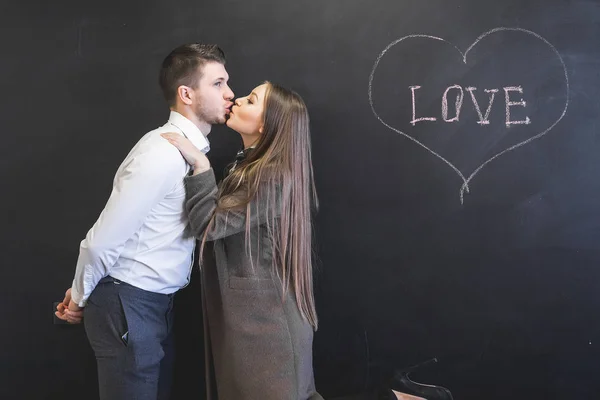 Jeune couple amoureux embrasser, derrière le tableau noir — Photo