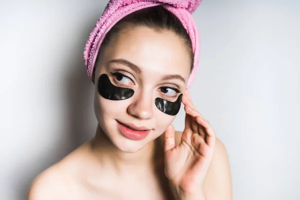 Menina bonita com uma toalha rosa na cabeça e com manchas de silicone preto no rosto sorrindo — Fotografia de Stock