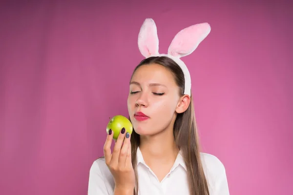 Bella ragazza in camicia bianca e in un orlo sotto forma di orecchie di coniglio mangiare una mela verde — Foto Stock