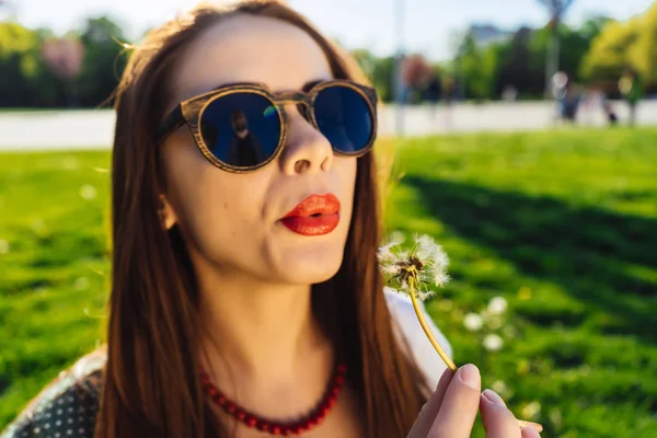 Komik gülümseyen mutlu kadın karahindiba üfleme güneş gözlüğü