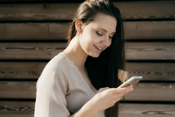 Giovane bella ragazza ridente in abito beige guardando nel suo smartphone — Foto Stock