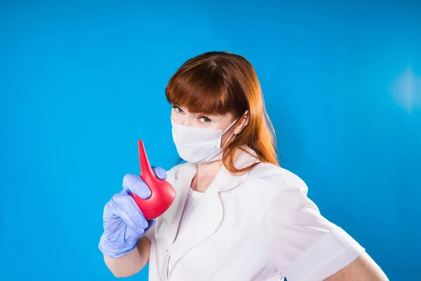 Mujer adulta médico en máscara médica y vestido tiene un enema rojo en las manos — Foto de Stock