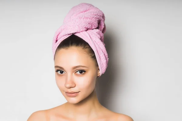 Vacker ung flicka med ren hud, med en rosa handduk på huvudet leende och tittar på kameran — Stockfoto