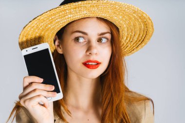 Kızıl saçlı genç kız bir hasır şapka ve kırmızı ruj ile bir akıllı telefon elinde tutan ve bir kenara görünüyor
