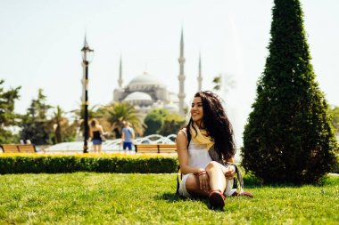 Parlak bir Türk kızı Istanbul'da Sultanahmet Camii arka plan çimlerde oturuyor