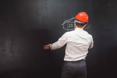 Beyaz bir gömlek ve bir portakal koruyucu kask adam Builder'da tebeşir bir ev bir tahtaya çizer.
