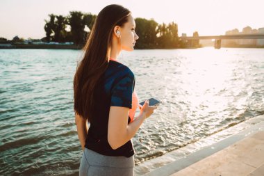 uzun saçlı kız güneşin, nehrin yanında ayakta kulaklıklar müzik spor