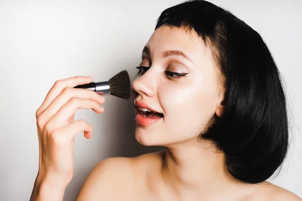 Bela menina atraente com cabelo preto faz maquiagem com uma escova cosmética — Fotografia de Stock
