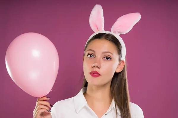 Een jong mooi meisje met een rand in de vorm van Haas oren houdt in haar hand een roze luchtballon — Stockfoto
