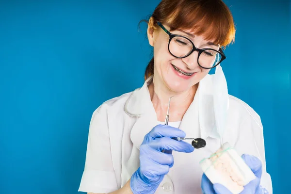 Yetişkin kadın doktor gözlük ve beyaz tıbbi paltolu gülümsüyor ve tıp aletleri elinde tutan — Stok fotoğraf