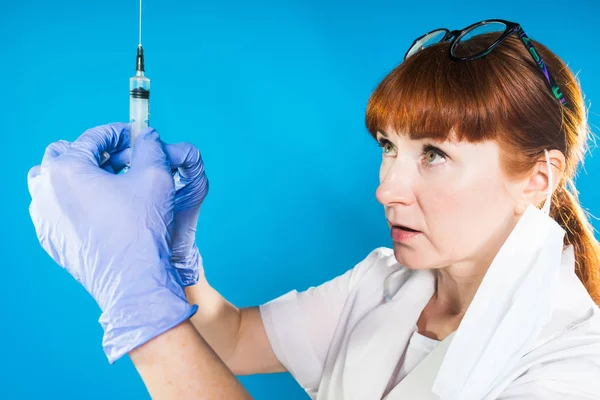 Médico adulto pelirrojo con gafas y guantes de goma azul sostiene una jeringa en las manos — Foto de Stock