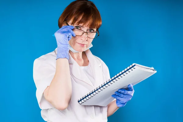 Adulto esperto medico donna in guanti di gomma blu tiene una cartella con documenti e si mette gli occhiali — Foto Stock
