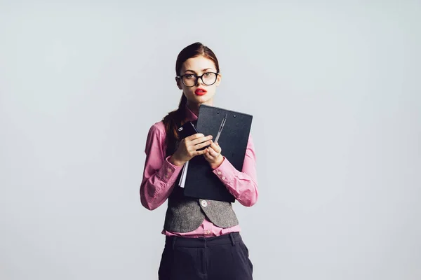 Ein modernes junges Mädchen mit Brille und rosa Hemd hält einen Ordner mit Dokumenten in der Hand und sieht müde und traurig aus — Stockfoto