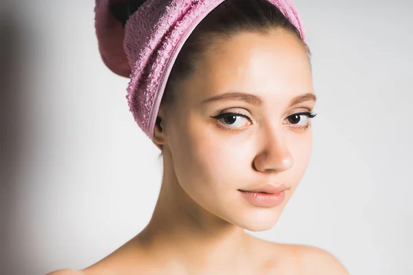 Schönes junges Mädchen mit sauberer Haut und einem rosa Handtuch auf dem Kopf, das in die Kamera schaut — Stockfoto