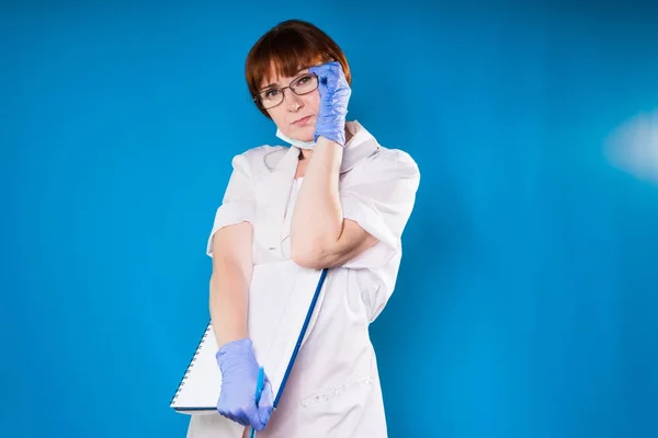 Adult red-haired woman doctor wearing glasses, wearing blue gloves holds notebook — Stock Photo, Image