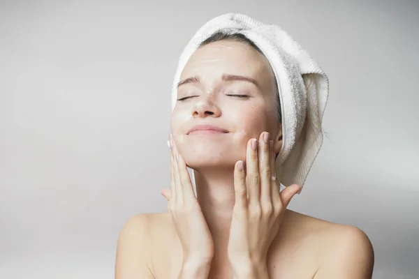 Happy young girl with clean skin and with a white towel on her head washes face — Stock Photo, Image