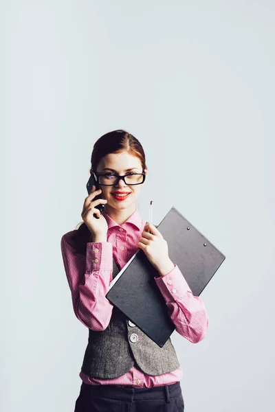 Stylisch lächelndes Mädchen mit Brille und rotem Lippenstift, das am Telefon spricht und Ordner mit Dokumenten in der Hand hält — Stockfoto