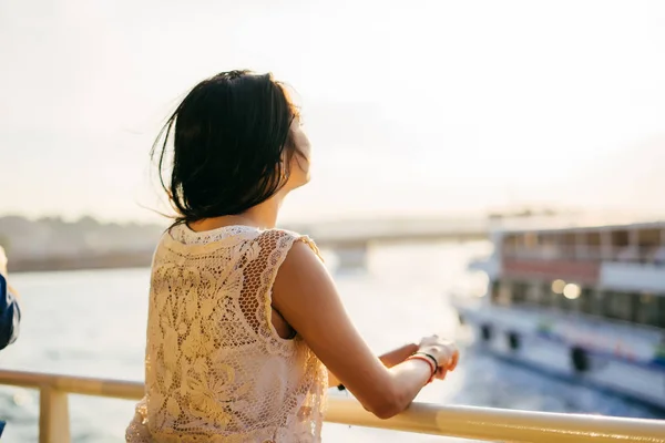 Una ragazza viaggia in nave sull'acqua al tramonto, si alza con la schiena, si gode il tramonto — Foto Stock