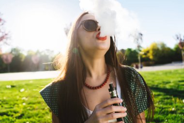Mutlu moda gülümseyen kadın güneş gözlüğü vape Street, duman Sigara