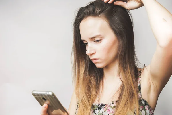 Hosszú hajú fiatal lány elgondolkozva néz ő okostelefon — Stock Fotó