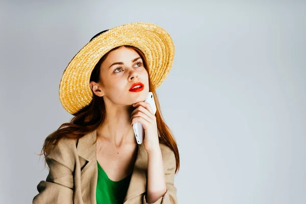 スタイリッシュなかわいい女の子麦藁帽子と赤い口紅、スマート フォンを保持して思慮深く見上げる — ストック写真