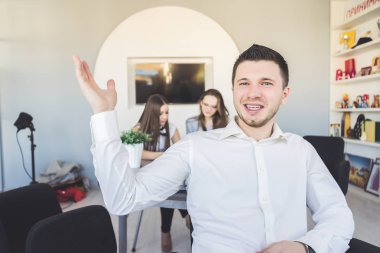 gülümseyen, onun arkasında 2 kız çalışma ofisinde oturan genç şık adam
