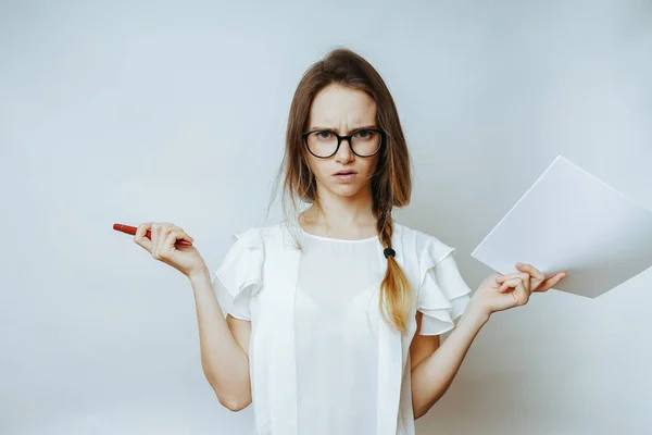 Сердитая девушка в очках держит листы бумаги и ручки, смотрит в камеру — стоковое фото