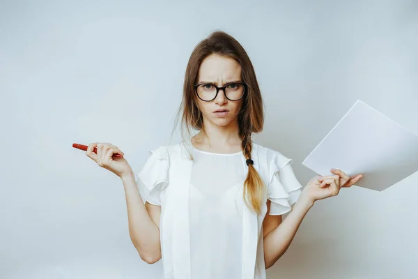 Wütendes junges Mädchen mit Brille hält Blatt Papier und Stift in der Hand, blickt in die Kamera — Stockfoto