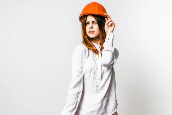 Uma jovem garota séria em uma camisa branca e um capacete protetor laranja olha em algum lugar — Fotografia de Stock