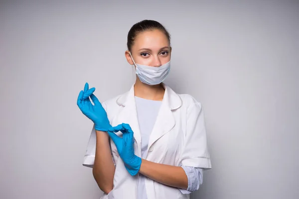 Söt ung kvinna läkare i medicinsk skyddsmask sätter på handskar — Stockfoto