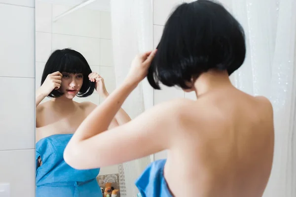 Красивая привлекательная девушка с черными волосами смотрит на себя в зеркало — стоковое фото