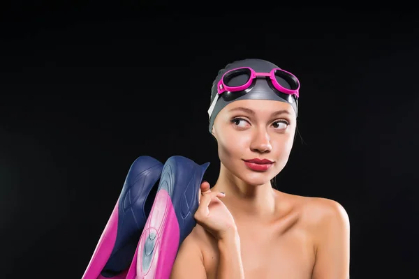 Confident young woman swimmer in a swimming cap and glasses holding flippers and smiling — Stock Photo, Image
