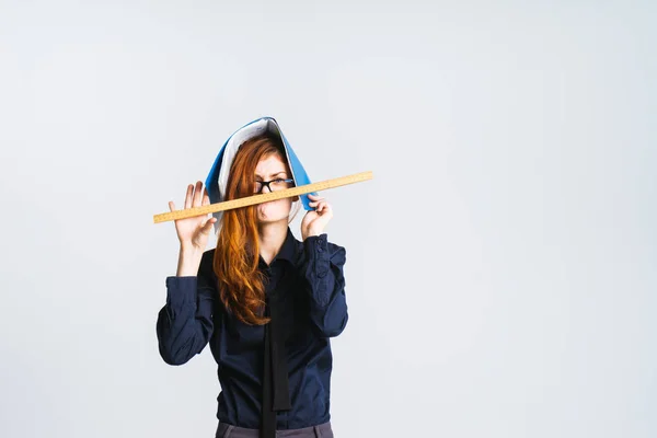 Een vreemde roodharige meisje met bril, ze heeft een map op haar hoofd, houdt een liniaal in de buurt van haar mond — Stockfoto