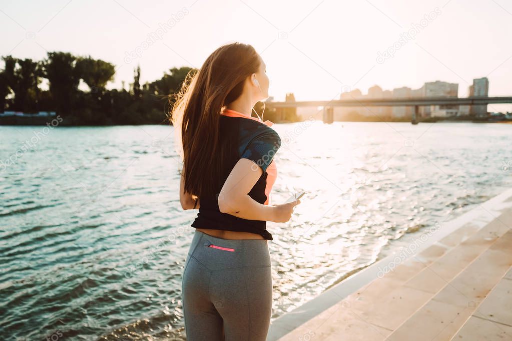 long-haired girl runs by the river at sunset, listens to music on headphones