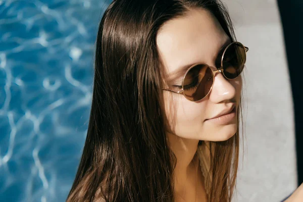 Bella ragazza in occhiali da sole seduto vicino all'acqua blu — Foto Stock