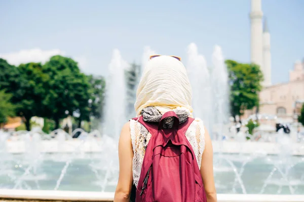 An unrecognizable woman in a scarf with a backpack on the background of a mosque and a fountain. Summer vacation, traveler — Stock Photo, Image