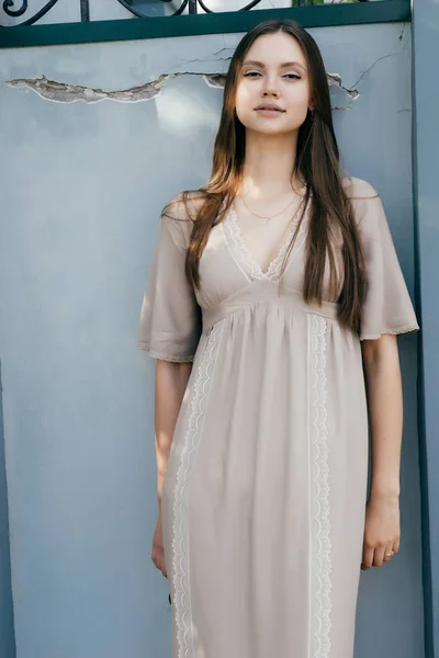 Bela menina encantadora em vestido bege posando contra a parede, sorrindo — Fotografia de Stock