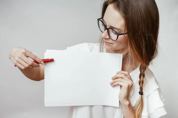 Mädchen mit Brille und weißem T-Shirt, das ein weißes Blatt a4 zeigt, in der Hand einen Stift — Stockfoto