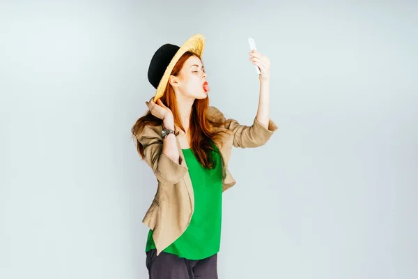 Una ragazza divertente elegante in un cappello di paglia e un maglione verde fa selfie — Foto Stock