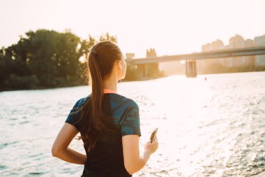 Spor fitness kız nehirde gün batımında kulaklık ile çalışır