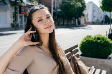 Kameraya bakarak da telefonda konuşurken güzel çekici kız bej elbise ve bir bankta oturan güneş gözlüğü