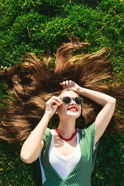 Mladá dívka v brýlích, sluneční brýle, na trávu, pohled nad, nahoře. Zdravý úsměv — Stock fotografie