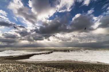 Mavi gökyüzü gri bulutlar üzerinde okyanus öfkeleniyor yakınındaki kayalık sahil