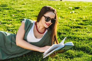 Okuma kadınla çimenlerin üzerinde. Öğrenci park, güneş gözlüğü hazırlanıyor